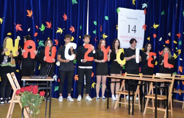 uczniowie stoją trzymając literki, które tworza napis nauczyciel